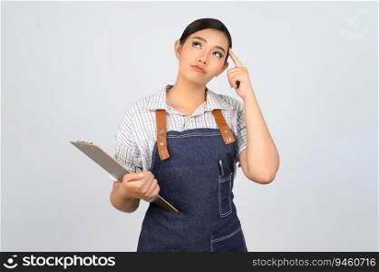 Portrait of young asian woman in waitress uniform holding clipboard and thinking pose, copy space to insert products for advertisement isolated on white background