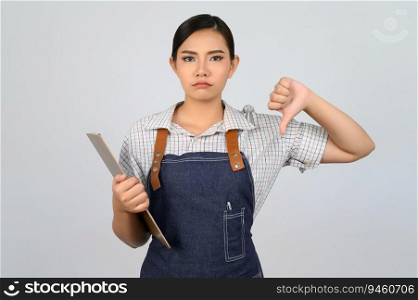 Portrait of young asian woman in waitress uniform holding clipboard and thumb down with upset pose, copy space to insert products for advertisement isolated on white background