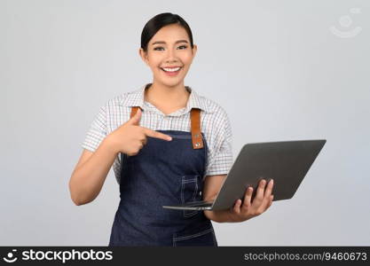 Portrait of young asian woman in waitress uniform pointing finger on laptop computer posture, copy space to insert products for advertisement isolated on white background