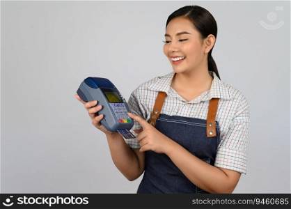 Portrait of young asian woman in waitress uniform pose with credit card and credit card reader machine in hand, copy space to insert products for advertisement isolated on white background