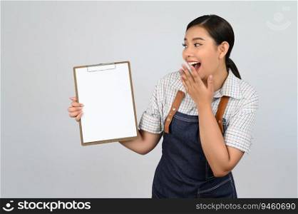 Portrait of young asian woman in waitress uniform showing mock up clipboard in hand with smile, copy space to insert text for advertisement isolated on white background