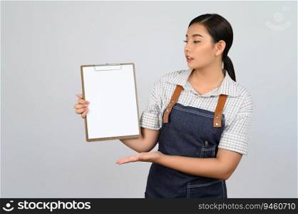 Portrait of young asian woman in waitress uniform showing mock up clipboard in hand with smile, copy space to insert text for advertisement isolated on white background