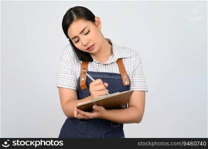Portrait of young asian woman in waitress uniform talking on smartphone and write order on clipboard during work, copy space for insert products for advertisement isolated on white background
