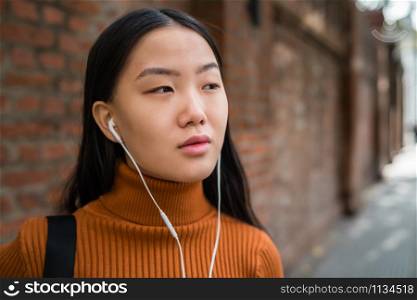 Portrait of young Asian woman listening to music with earphones in the street. Outdoors.