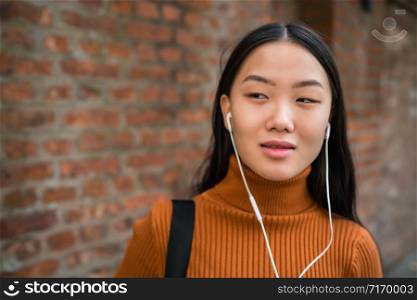 Portrait of young Asian woman listening to music with earphones in the street. Outdoors.