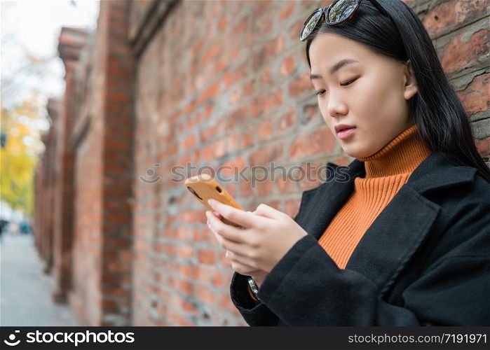 Portrait of young Asian woman using her mobile phone outdoors in the street. Urban and communication concept.