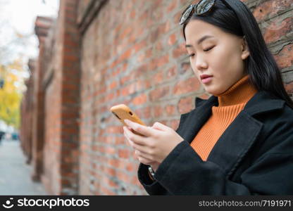 Portrait of young Asian woman using her mobile phone outdoors in the street. Urban and communication concept.
