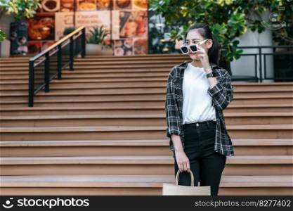 Portrait of young Asian woman wearing eyeglasses going down stairs with shopping paper bag. she smile and looking at camera,  Lifestyle and shopping concept, Shopping selection