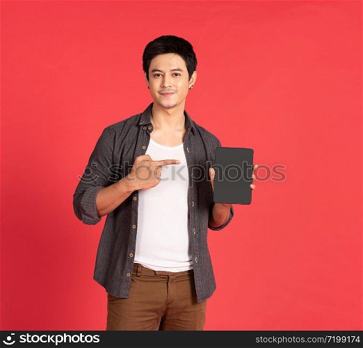 Portrait of young attractive asian businessman or student using mobile phone, laptop, tablet, standing isolated on red background wearing casual shirt look at camera in studio with copy space.