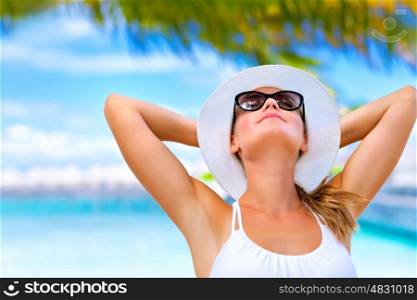 Portrait of young attractive female with hands behind head taking sunbath on the beach, summer vacation on Maldives