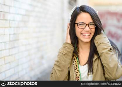 Portrait of young attractive girl in urban background hearing music with headphones