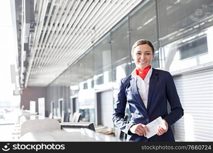 Portrait of young attractive passenger service agent holding boarding pass in airport check in area