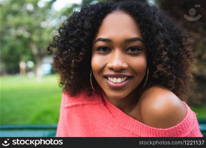 Portrait of young beautiful afro american woman sitting on bench in the park. Outdoors.