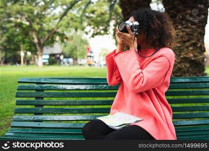 Portrait of young beautiful afro american woman using a professional camera while holding a map in a park. Travel concept.