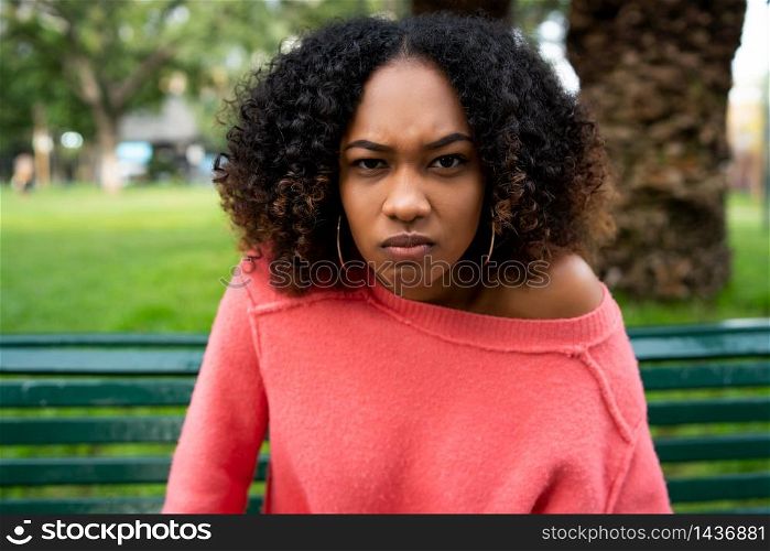 Portrait of young beautiful afro american woman with angry expression sitting on bench in the park. Outdoors.