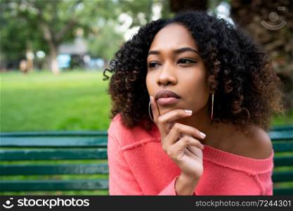 Portrait of young beautiful afro american woman with thoughtful expression sitting on bench in the park. Outdoors.