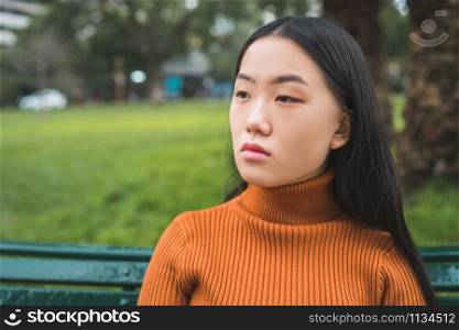 Portrait of young beautiful Asian woman sitting on a bench in the park outdoors.