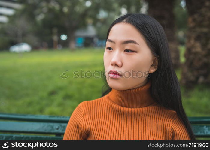 Portrait of young beautiful Asian woman sitting on a bench in the park outdoors.