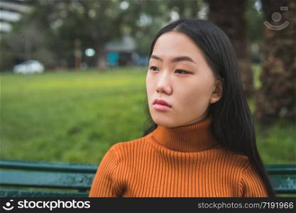 Portrait of young beautiful Asian woman sitting on a bench in the park outdoors.