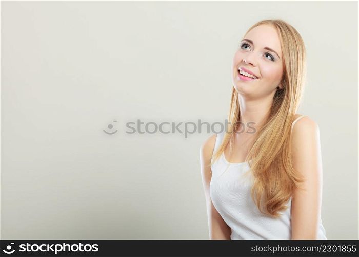 Portrait of young beautiful blonde woman smiling and looking up on gray background