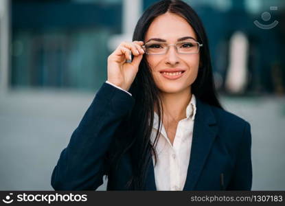 Portrait of young, beautiful business woman in glasses and suit. Modern building, financial center, cityscape. Successful female businessperson