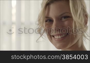 Portrait of young beautiful caucasian blonde woman turning head and smiling at camera. Slow motion, copy space
