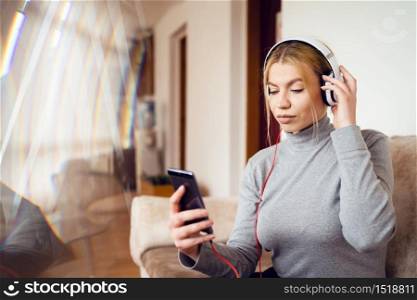 Portrait of young beautiful caucasian woman with earphones sitting in hotel - One alone adult happy blonde female listen to music in day - Waist up front view - Happiness enjoyment and joy concept