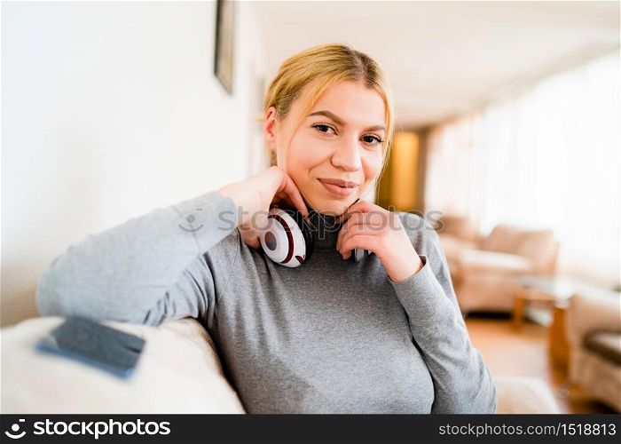 Portrait of young beautiful caucasian woman with earphones sitting in hotel - One alone adult happy blonde female looking to camera in day - Waist up front view - Happiness enjoyment and joy concept