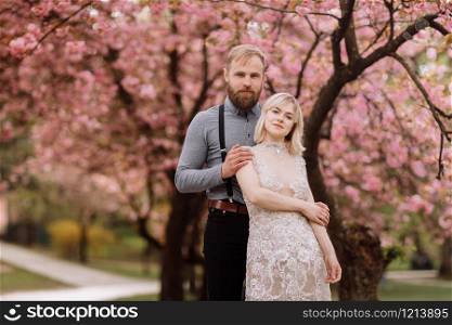 portrait of young beautiful couple in blossoming pink cherry blossom, sakura garden and hugging on a sunny day. Spring wedding portrait. valentine&rsquo;s day. portrait of young beautiful couple in blossoming pink cherry blossom, sakura garden and hugging on a sunny day. Spring wedding portrait. valentine&rsquo;s day.