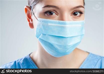 Portrait of young beautiful female EMS medical worker,wearing blue uniform and protective face mask,studio headshot isolated on white background,stress and worry due to Coronavirus COVID-19 pandemic