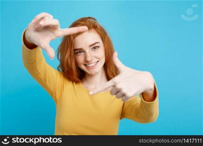 Portrait of young beautiful ginger woman with freckles cheerfuly smiling making a camera frame with fingers. Isolated on white background. Copy space.