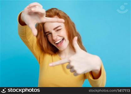 Portrait of young beautiful ginger woman with freckles cheerfuly smiling making a camera frame with fingers. Isolated on white background. Copy space.
