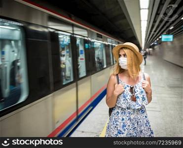 Portrait of young beautiful girl in disposable face mask waits for train on subway platform. Concept of prevention and social distancing in coronavirus,covid19 pandemic. Young beautiful woman waiting for train during epidemic