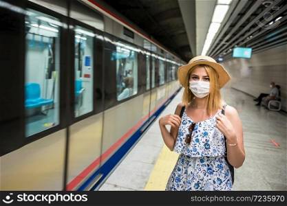 Portrait of young beautiful girl in disposable face mask waits for train on subway platform. Concept of prevention and social distancing in coronavirus,covid19 pandemic. Young beautiful woman waiting for train during epidemic