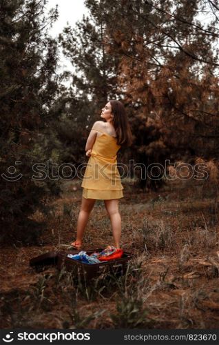 portrait of young beautiful girl in yellow dress with colorful scarf changing clothes in the forest in the rain