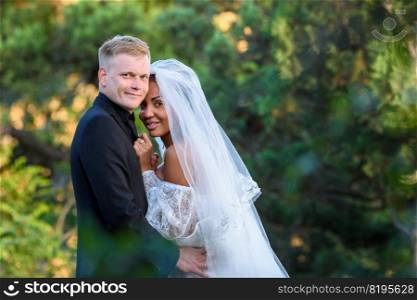 Portrait of young beautiful interracial newlyweds on green foliage background