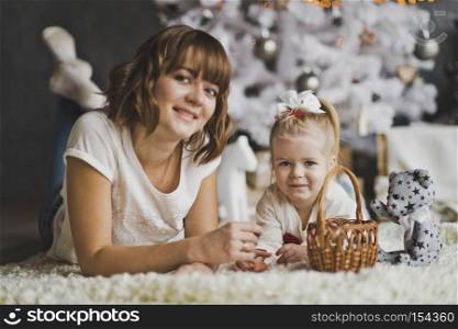 Portrait of young beautiful mother with her little daughters Christmas tree.. Mother and daughter lying on the carpet under white decorated Christmas tree 7129.