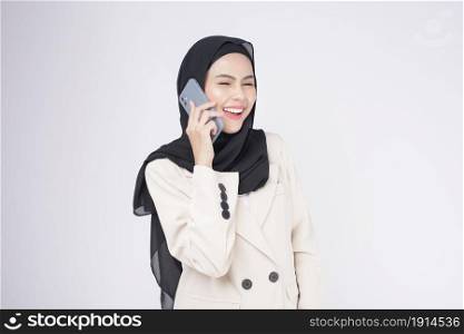 Portrait of young beautiful muslim woman in suit using smart phone over white background