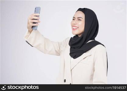 Portrait of young beautiful muslim woman in suit using smart phone over white background
