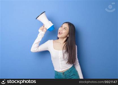 portrait of young beautiful smiling woman is using megaphone to announce over isolated blue background studio