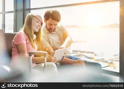 Portrait of young beautiful teenage girl showing digital tablet to her father while sitting and waiting for their flight in airport