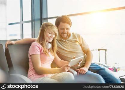 Portrait of young beautiful teenage girl showing digital tablet to her father while sitting and waiting for their flight in airport