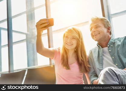 Portrait of young beautiful teenage girl taking selfie with her father in airport