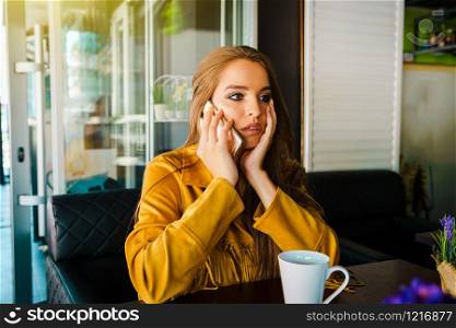 Portrait of young beautiful woman at cafe restaurant talking to the mobile phone call receiving disturbing surprising news face reacting hand over head holding