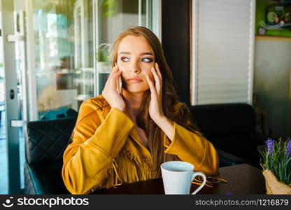 Portrait of young beautiful woman at cafe restaurant talking to the mobile phone call receiving disturbing surprising news face reacting