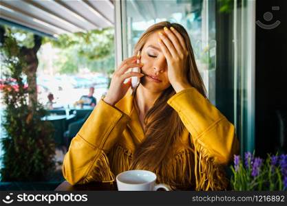 Portrait of young beautiful woman at cafe restaurant talking to the mobile phone call receiving disturbing surprising news holding her head with hand forehead