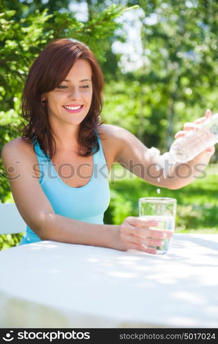 Portrait of young beautiful woman drinking water on picnic at summer green park.