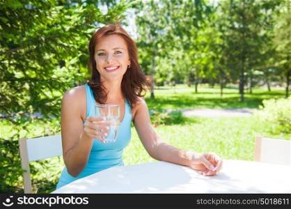 Portrait of young beautiful woman drinking water on picnic at summer green park.