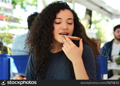 Portrait of young beautiful woman eating a toast while having breakfast at a coffee shop.