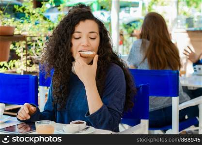Portrait of young beautiful woman eating a toast while having breakfast at a coffee shop.
